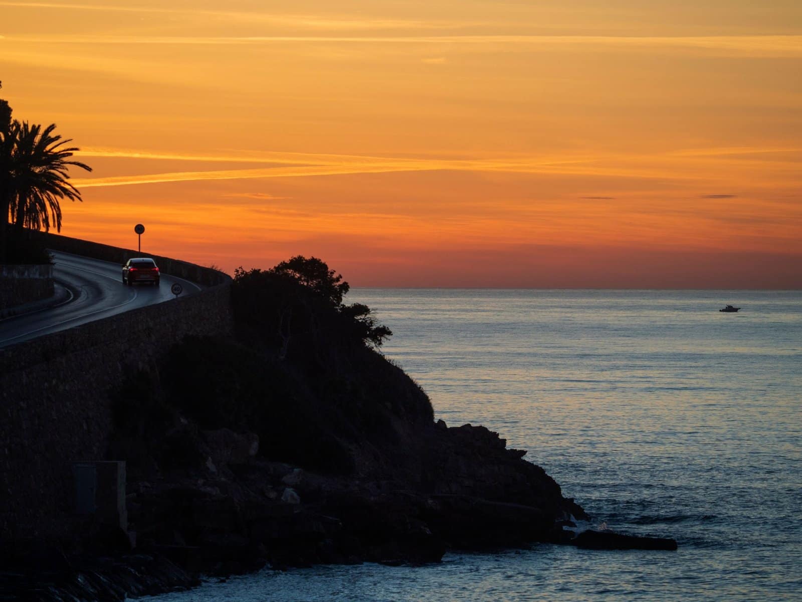 Orange Classic Car Driving Along a Coastal Sunset Road