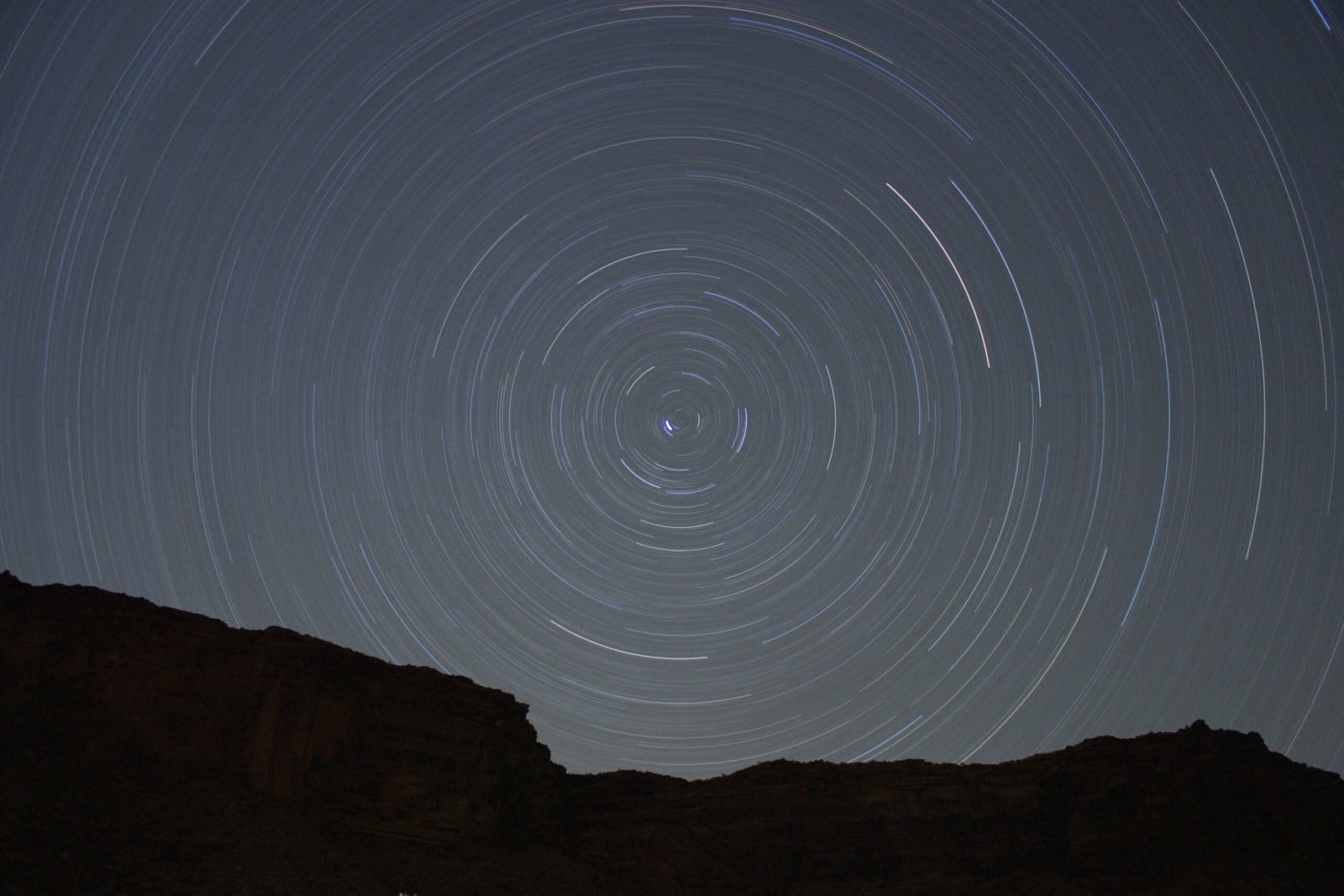 Star Trails Spiraling Over a Silhouetted Rock Face at Night