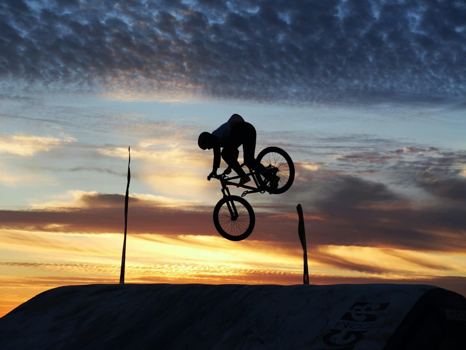 BMX Rider Flying Over Dirt Jump at Dusk